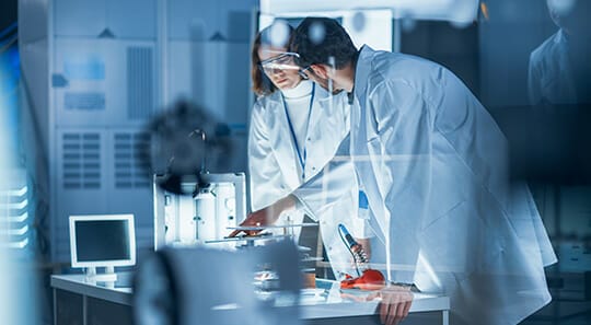 Diverse International Team of Industrial Scientists and Engineers Wearing White Coats Working on Heavy Machinery Design in Research Laboratory. Professionals Using 3D Printer, Computers and Microscope
